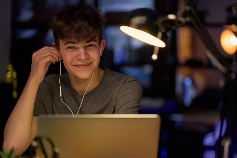 A young student with a laptop and headphones on, looking straight at the camera and smiling.