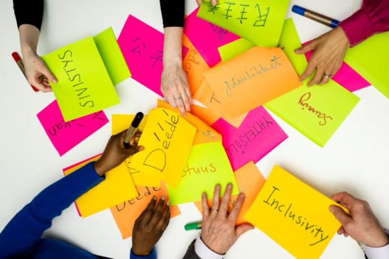 Pino värikkäitä paperilappuja, joissa eri kielillä vastuullisuussanastoa, kuten sivistys tai totuus. Tusseja ja monennäköisiä käsiä lappuja kirjoittamassa.