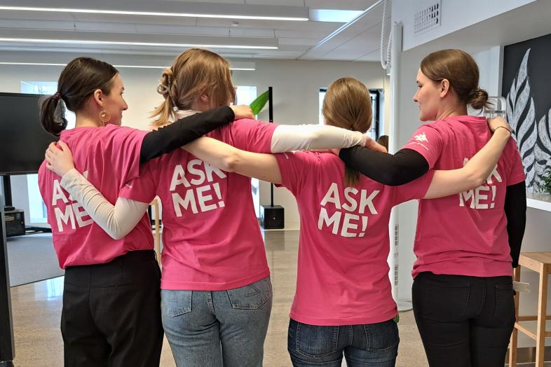 Neljä työntekijää Ask Me! -paidat päällä