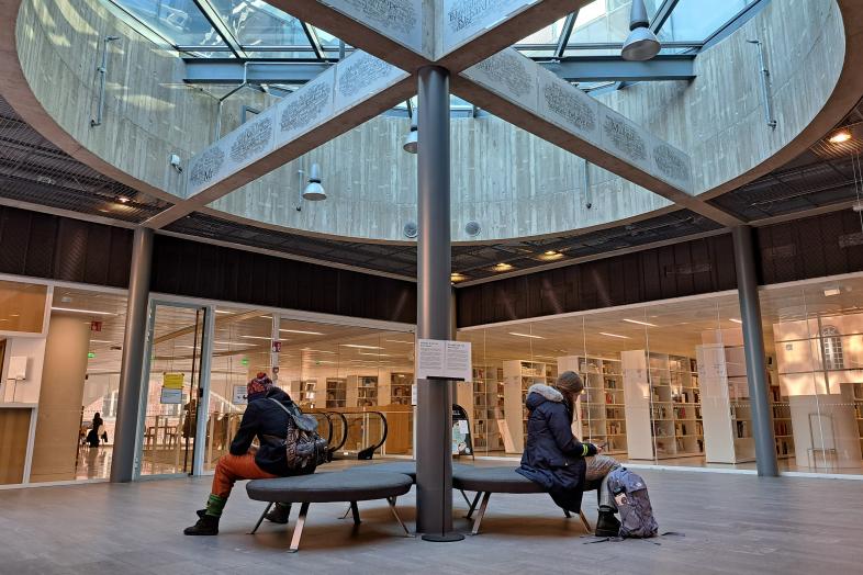 Kaksi opiskelijaa istuu selin toisiinsa Aleksandrian aulan penkeillä.