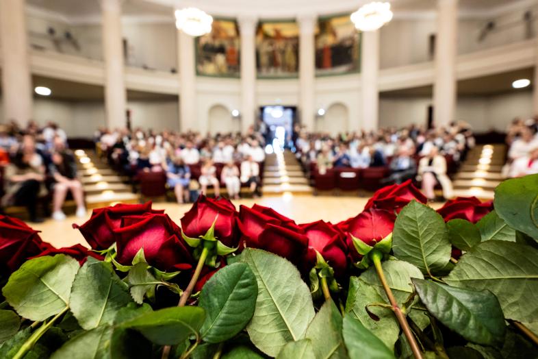 In the foreground a row of red roses, in the background the audience in the grandstand.