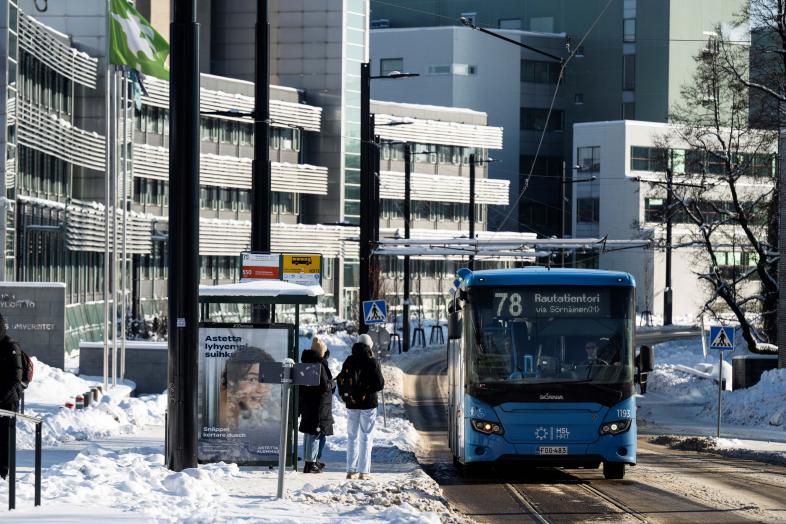 Ihmisiä nousemassa bussiin talvisessa Viikinkaaressa.