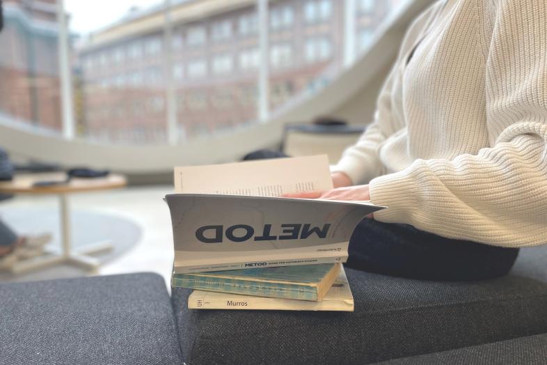 Henkilö selaamassa kirjoja penkillä Kaisa-talossa.