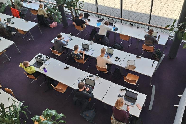 Henkilöitä työskentelemässä läppäreillä Kumpulan kampuskirjastossa ylhäältä kuvattuna.