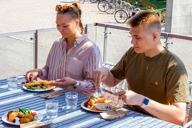 Kaksi henkilöä syömässä Unicafen lounasta ulkona.