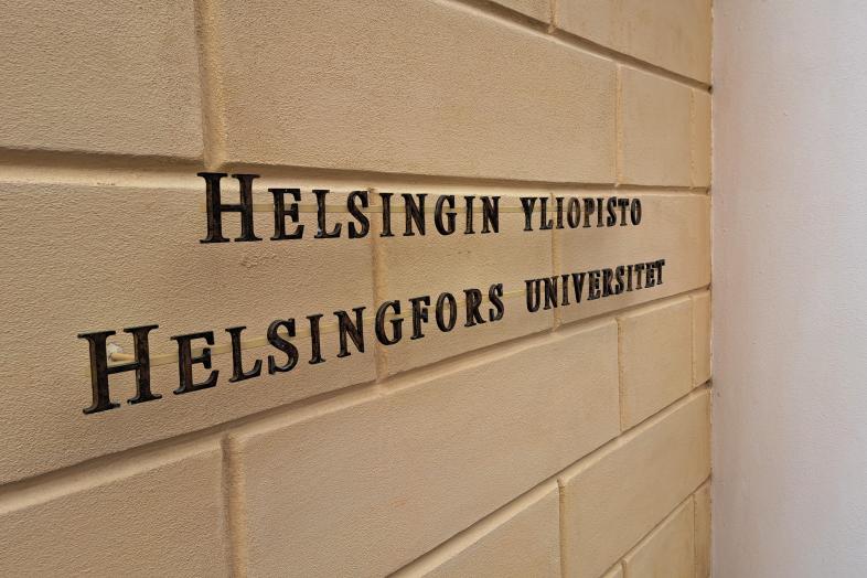 Keltaisella tiiliseinällä teksti Helsingin yliopisto, Helsingfors universitet.