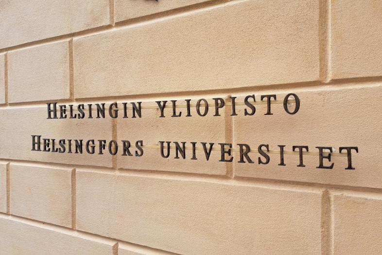 Keltaisella tiiliseinällä musta teksti "Helsingin yliopisto, Helsingfors universitet".