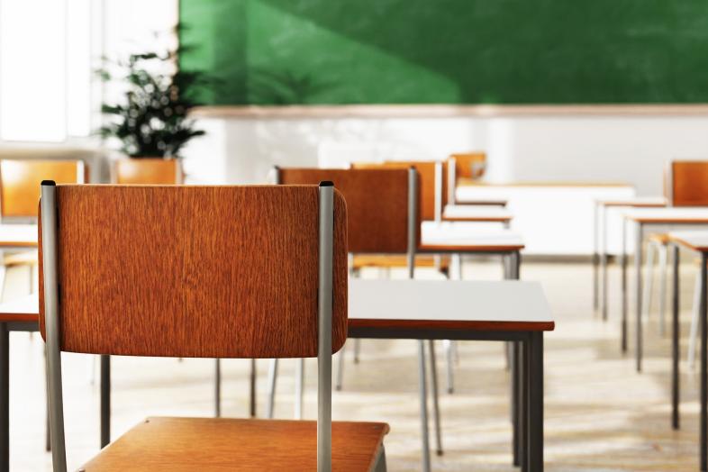 Koululuokka, jossa vihreä liitutaulu ja pöytiä ja tuoleja.
