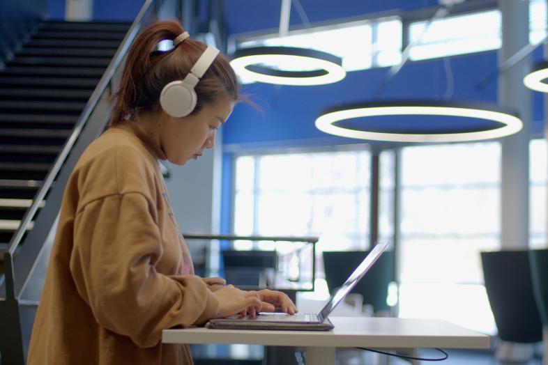 Opiskelija työskentelee kuulokkeet päässä kannettavalla tietokoneella.