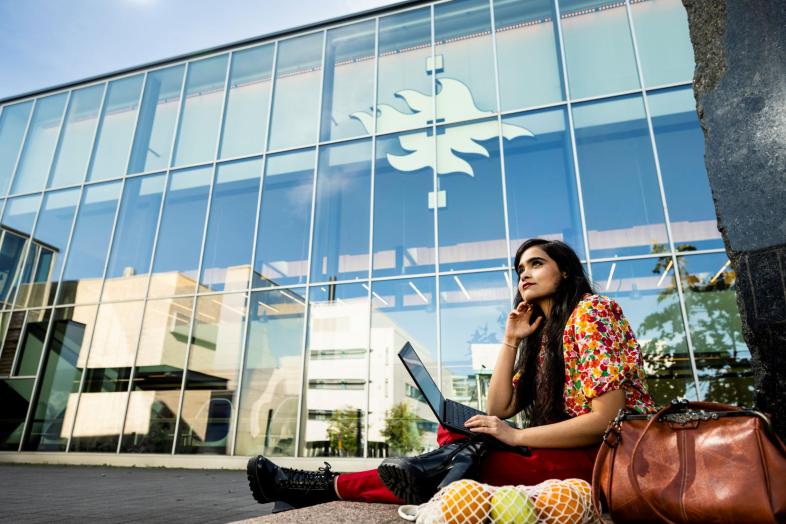 Henkilö työskentelee puun alla Kumpulan Physicum-rakennuksen edessä.