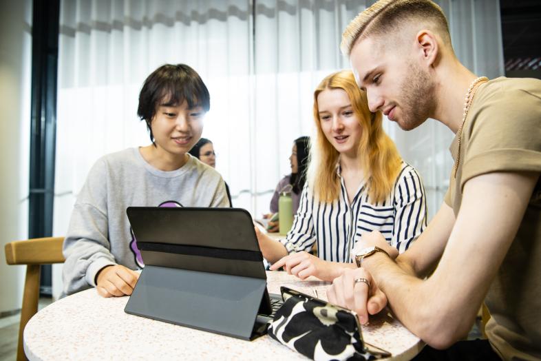 Three students around a table, working on a tablet.