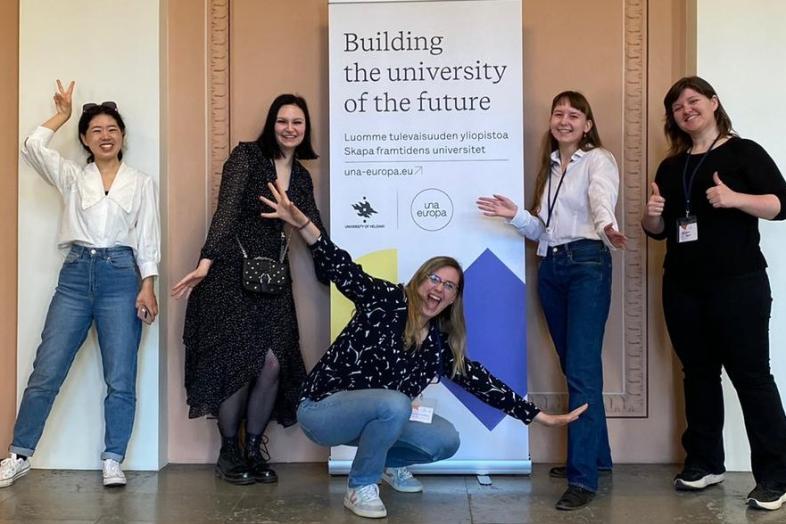 five students are smiling and standing in front of a roll-up