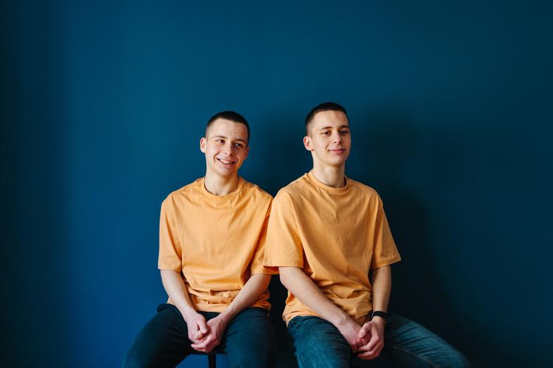 Kaksoset istuvat sinistä taustaa vasten oranssit t-paidat päällään.