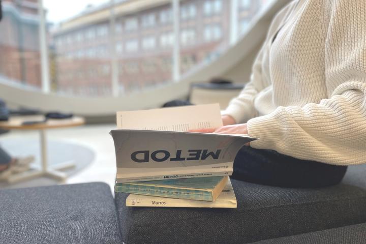 Henkilö selaamassa kirjoja penkillä Kaisa-talossa.