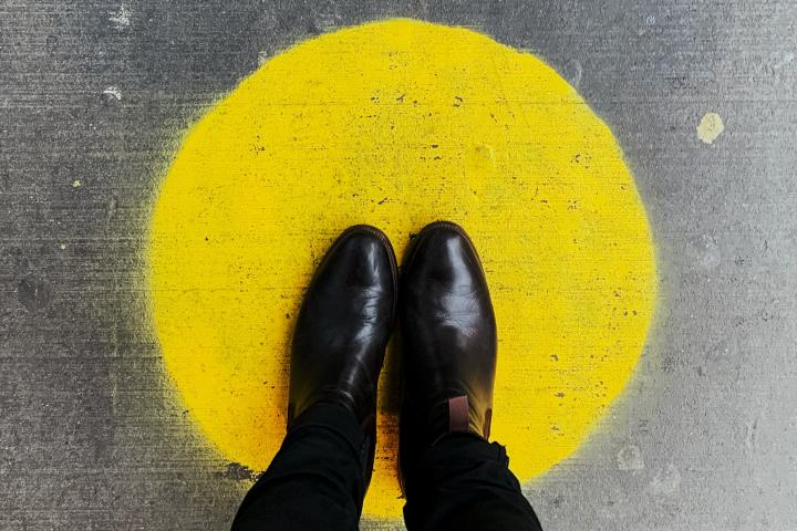 Kuvituskuva, jossa mustakenkäinen henkilö seisoo lattiaan maalatun keltaisen ympyrän keskellä.